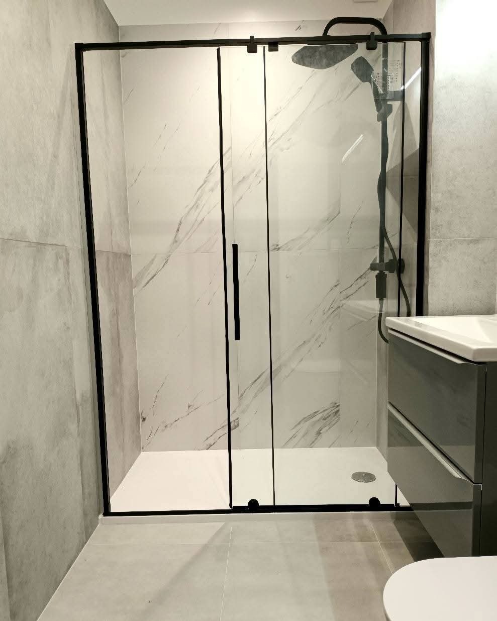 Nowoczesna kabina prysznicowa z czarnymi ramami i marmurowymi płytkami w łazience. Widoczna umywalka z szafką. Minimalistyczny design, jasne wnętrze.