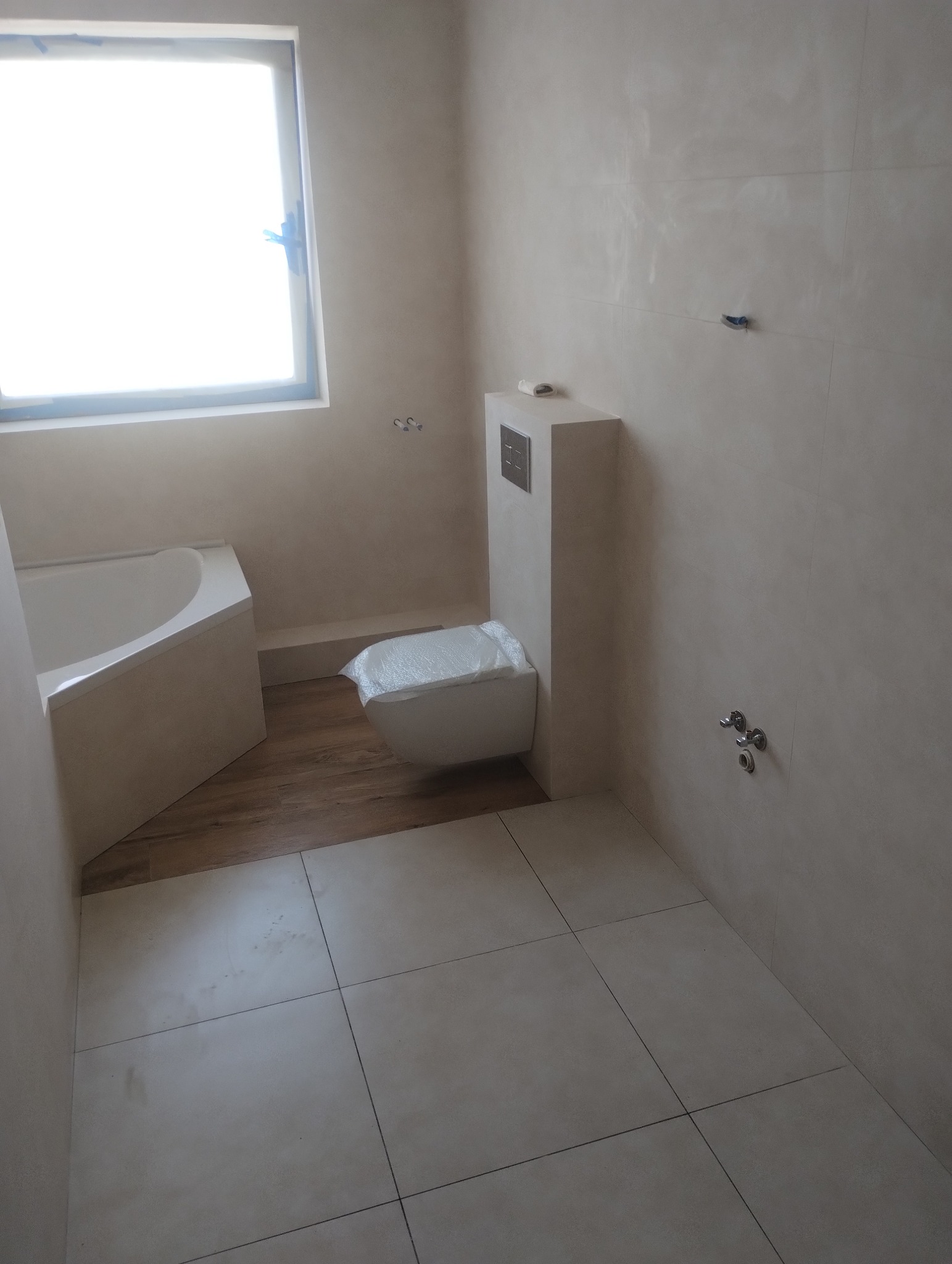 Wykończona łazienka w Szczecinie: beżowe płytki podłogowe i ścienne, podwieszana toaleta z zabudową, wanna przy oknie. Minimalistyczny design.