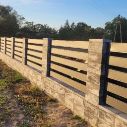 Dominik Chmielewski - Nowoczesne ogrodzenie panelowe z betonową podmurówką, widok z boku na tle zieleni i budynku. Słoneczny dzień, wyraźne detale konstrukcji.