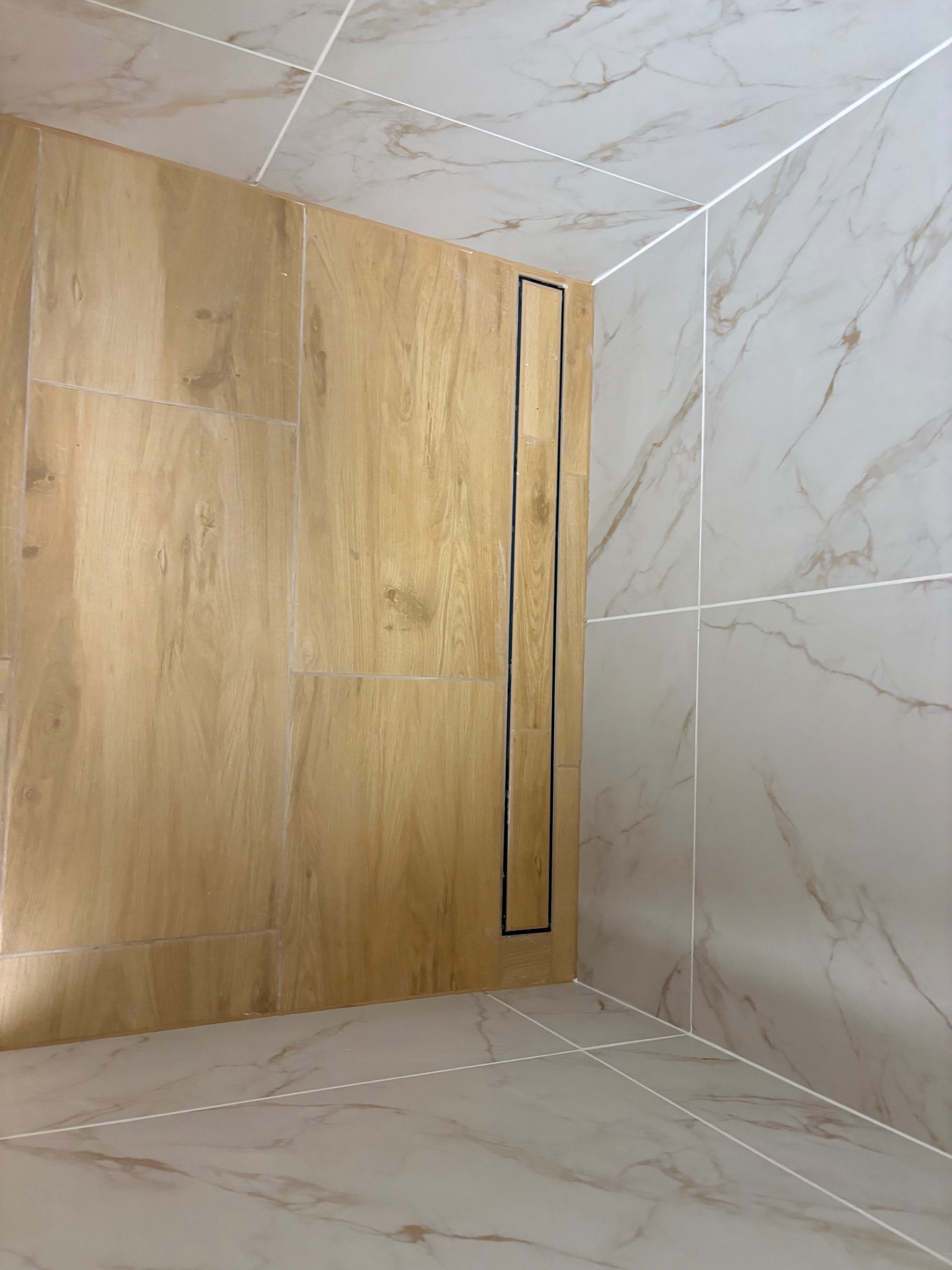 Wykończona kabina prysznicowa z odpływem liniowym i płytkami imitującymi drewno w Dąbiu. Marmurowe płytki na ścianach i podłodze. Nowoczesny design.