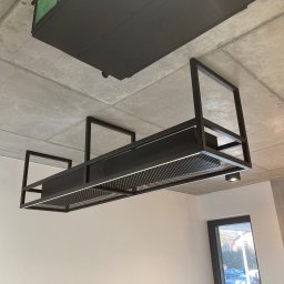 Tomasz Sekuła MetalFusion - Nowoczesna, czarna, metalowa konstrukcja sufitowa z oświetleniem LED, widoczna na tle surowego, betonowego sufitu i białych ścian. Minimalistyczny design.