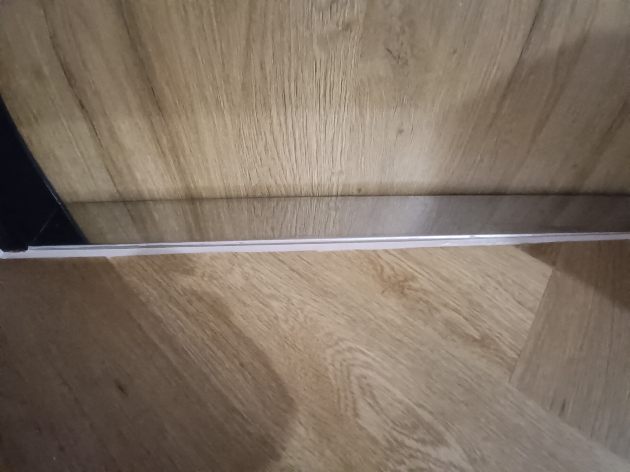 Ułożone panele podłogowe w jasnym odcieniu drewna, widoczne z bliska, z listwą przypodłogową. Minimalistyczne ujęcie detalu wykończenia wnętrza.