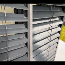 Piotr Kowalewski - Szare, aluminiowe żaluzje zewnętrzne po deszczu, z widocznymi kroplami wody. Ujęcie z bliska, ukazujące detale konstrukcji i świeżość po czyszczeniu.