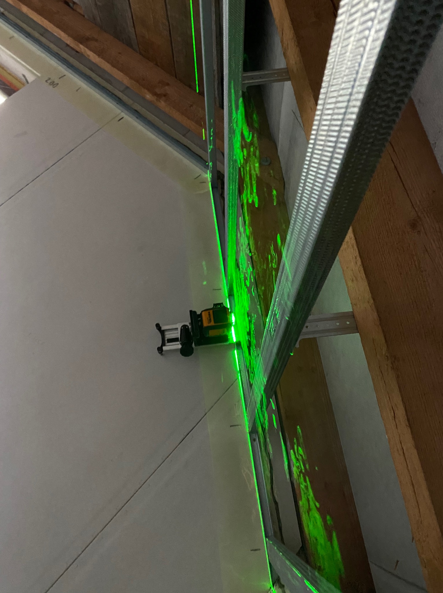 Montaż płyty gipsowej na poddaszu z użyciem poziomicy laserowej. Widoczne profile metalowe i drewniana konstrukcja dachu. Precyzyjne wyznaczanie linii cięcia.