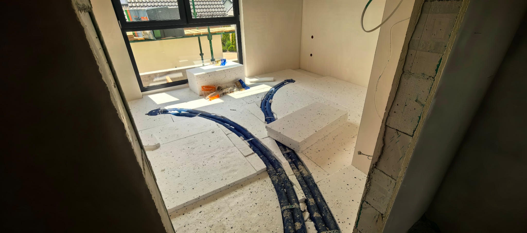 Wnętrze w trakcie prac wykończeniowych: izolacja podłogowa ze styropianu i rury ogrzewania podłogowego. Ściany przygotowane do dalszych prac. Widok na okno.