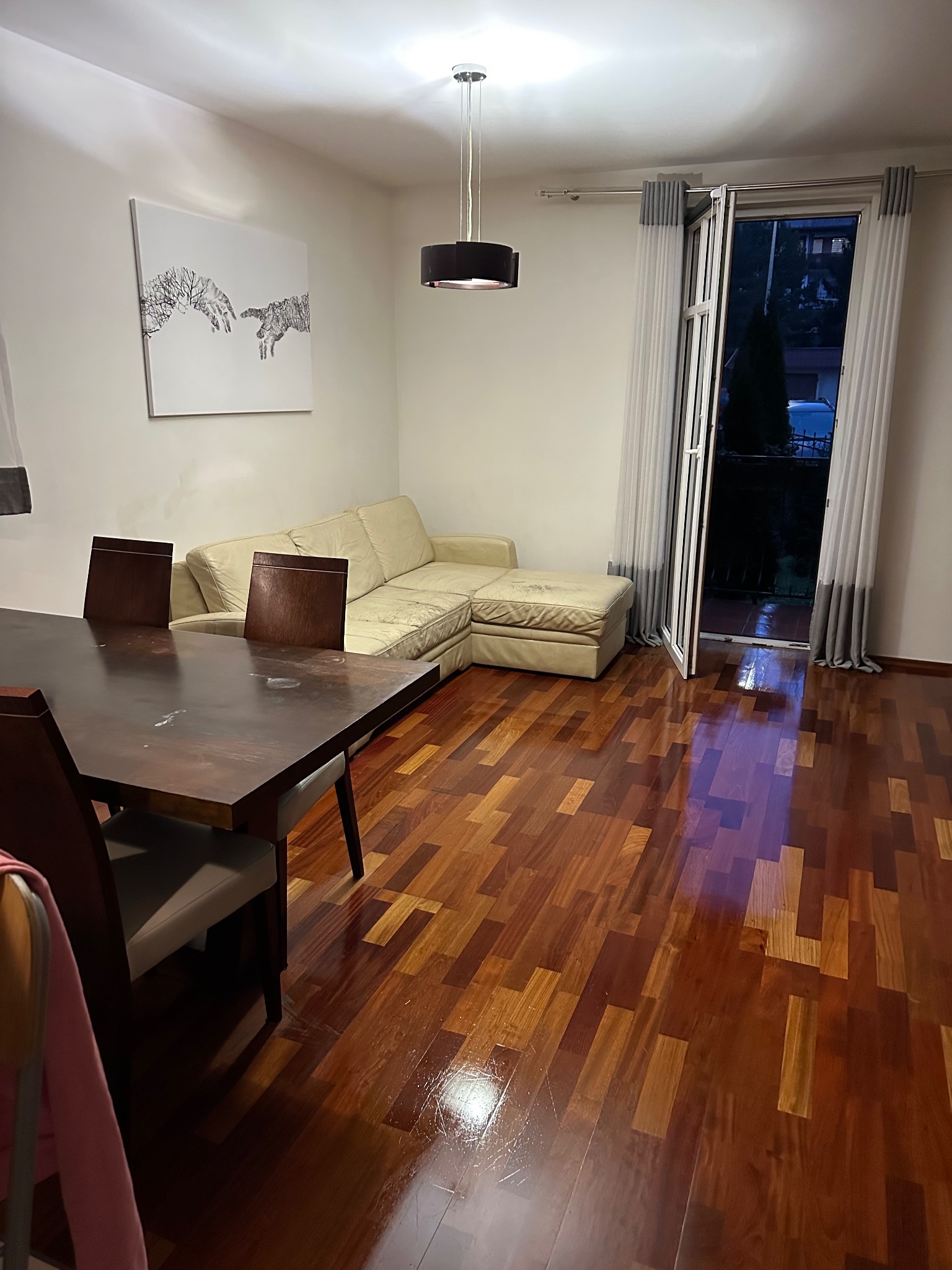 Salon z drewnianą podłogą po czyszczeniu, widoczny stół z krzesłami, kanapa i otwarte drzwi balkonowe z zasłonami. Na ścianie obraz.