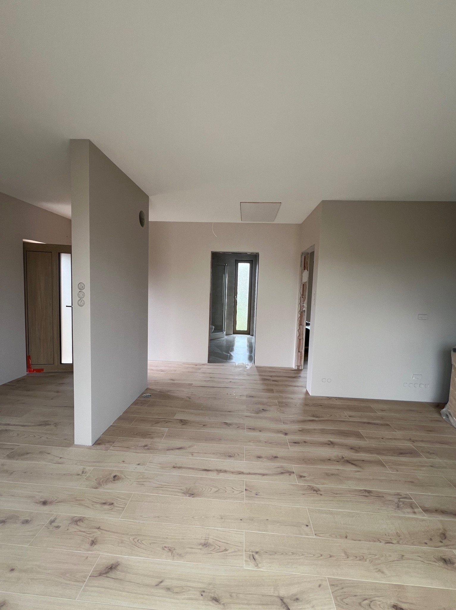 Jasne wnętrze po remoncie: drewnopodobna podłoga, świeżo pomalowane ściany w odcieniach beżu, widoczne drzwi i okna. Minimalistyczny design, gładkie powierzchnie.