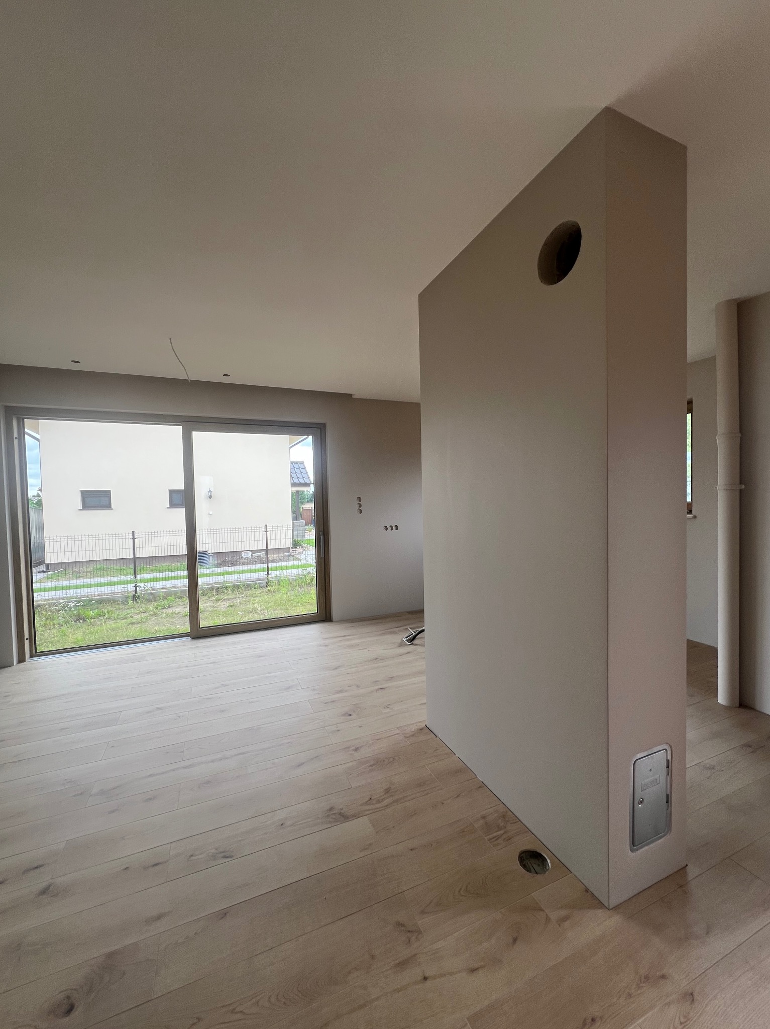 Jasne, przestronne wnętrze po remoncie z drewnianą podłogą, dużym oknem przesuwnym i ścianą z otworem wentylacyjnym. Minimalistyczny design, świeżo pomalowane ściany.