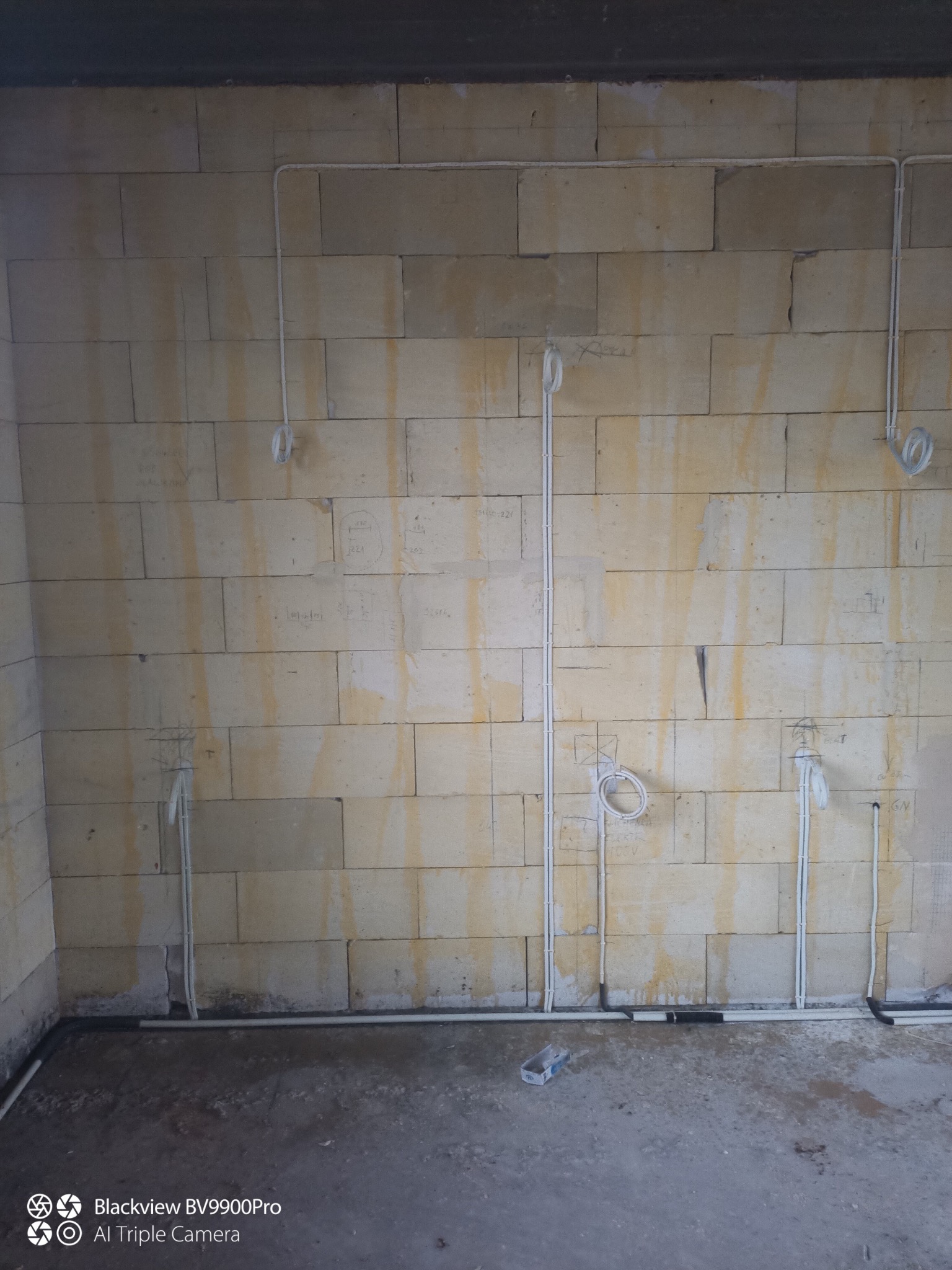 Ściana z pustaków z rozprowadzoną instalacją elektryczną w białych rurkach. Widoczne kable i puszki instalacyjne. Etap prac przed tynkowaniem.