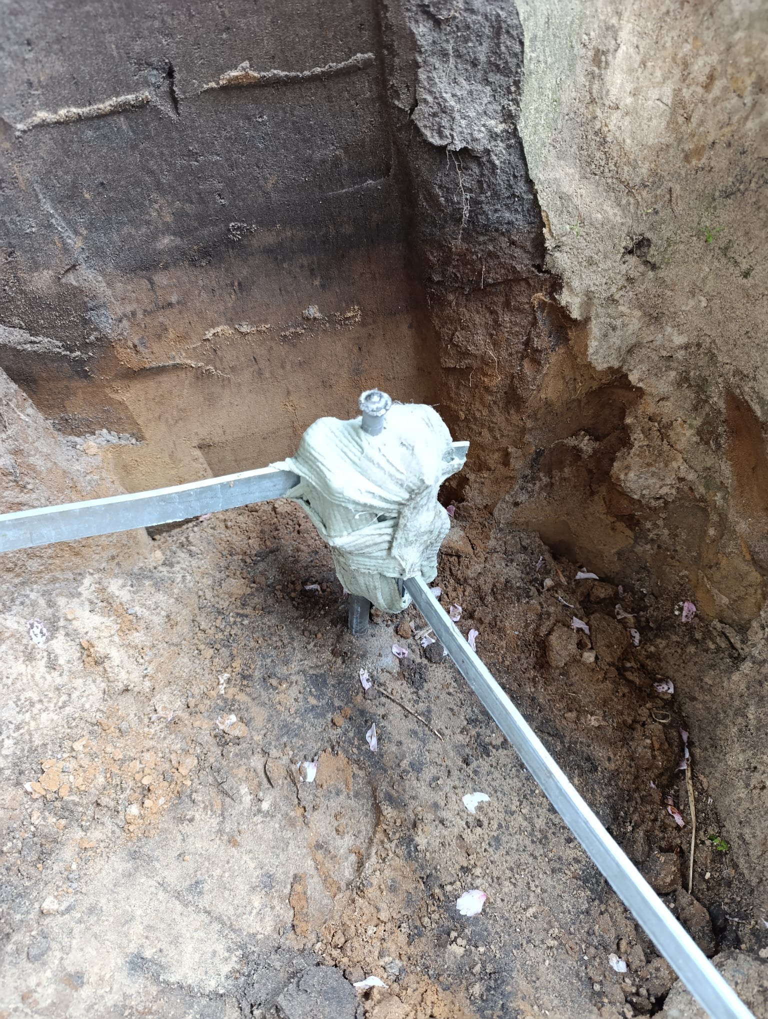 Uziemienie pionowe z bednarką w wykopie, zabezpieczone owijką. Widoczne ślady po kwitnących drzewach. Grunt piaszczysty.