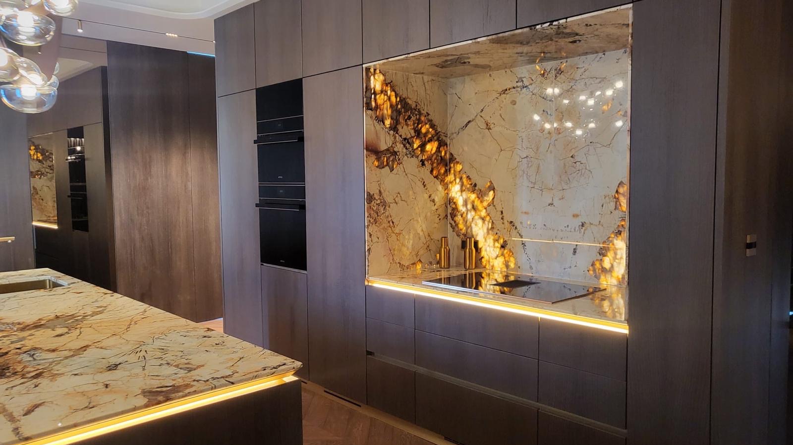 Nowoczesna kuchnia z szarymi szafkami i blatem z marmuru z podświetleniem LED. Na ścianie dekoracyjny panel z podświetlonym onyksem.