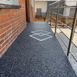 Green House - Wykończony taras kamienny z żywicy epoksydowej w kolorze grafitowym, z geometrycznym wzorem. Widoczne metalowe barierki i fragment elewacji z cegły.