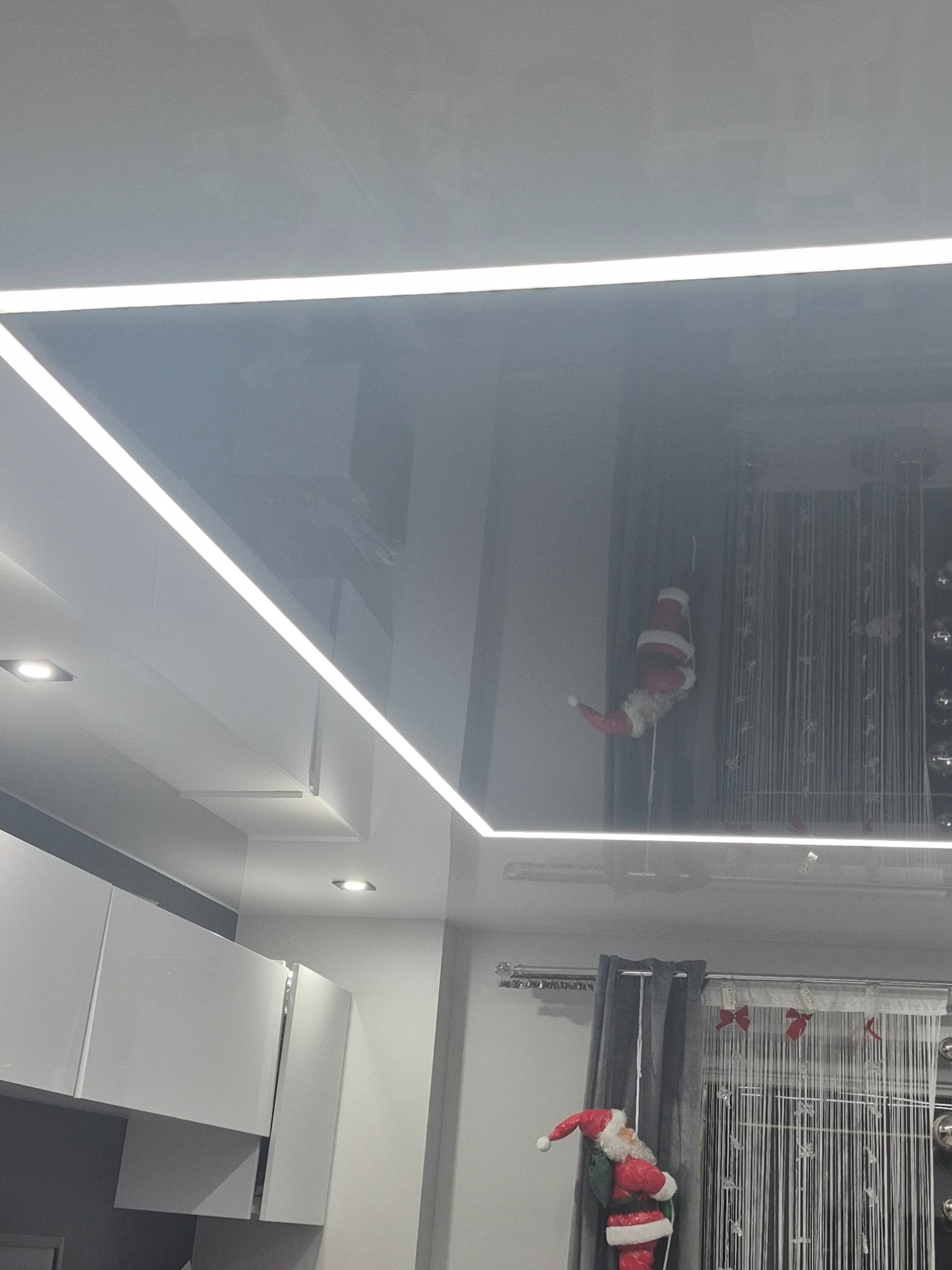 Błyszczący, czarny sufit napinany z oświetleniem LED wzdłuż krawędzi, odbijający elementy wystroju wnętrza, w tym dekoracje świąteczne.