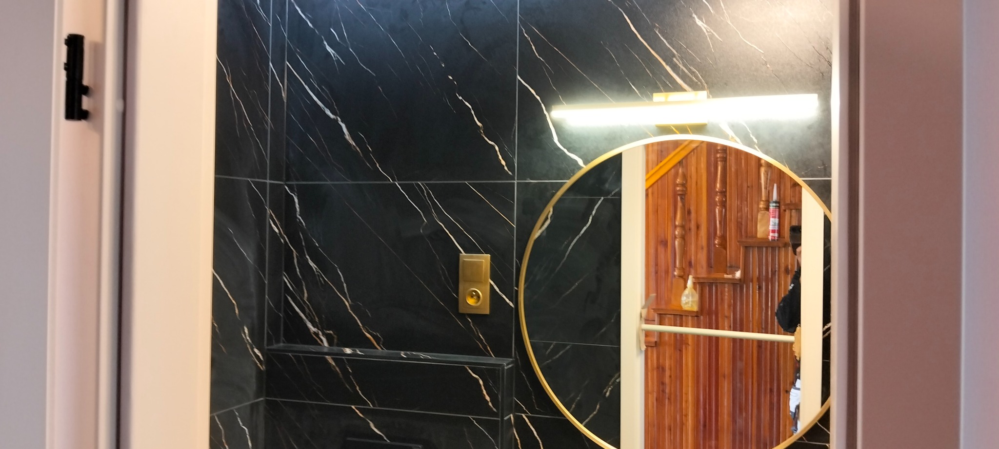 Czarne płytki imitujące marmur z złotymi żyłami i okrągłe lustro w łazience w Opatówku. Nowoczesne wykończenie wnętrz z oświetleniem.