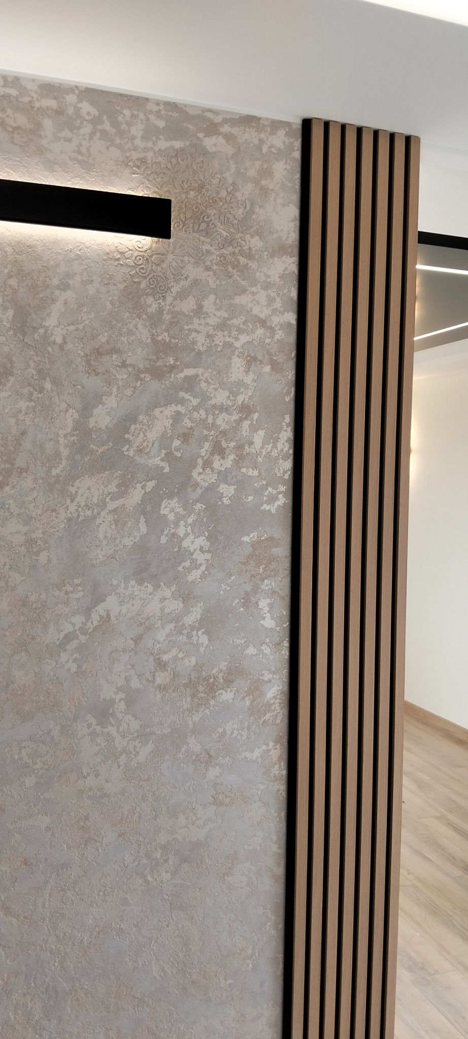 Dekoracyjna ściana z efektem betonu i drewniane lamele pionowe, oświetlenie punktowe. Nowoczesne wykończenie wnętrza, detale aranżacji.