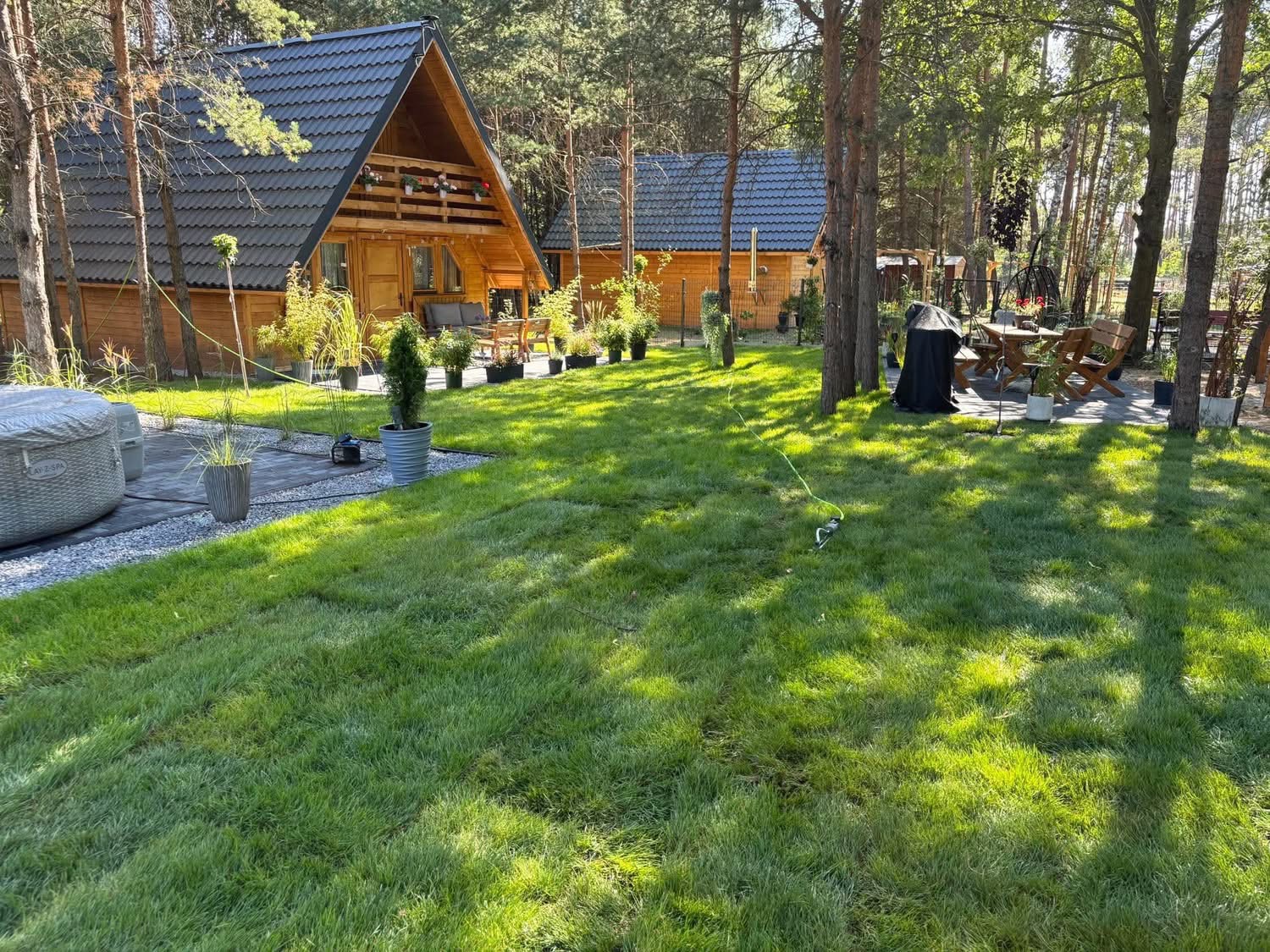 Ułożona trawa z rolki w ogrodzie z drewnianymi domkami, jacuzzi i meblami ogrodowymi. Widok na świeżo założony trawnik w słoneczny dzień.