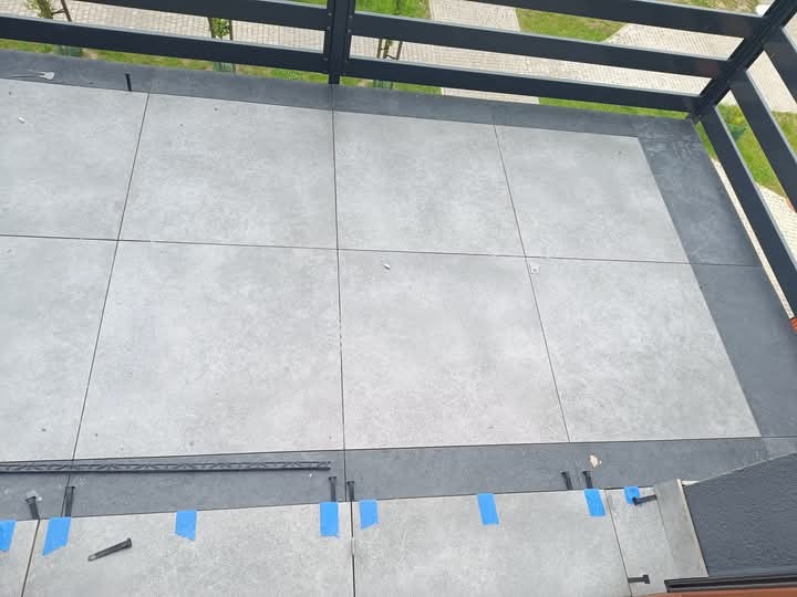 Jasnoszare płytki tarasowe ułożone pod zadaszeniem, widoczne niebieskie taśmy mocujące i elementy konstrukcyjne. Ujęcie z góry, podkreślające regularny wzór i nowoczesny wygląd.