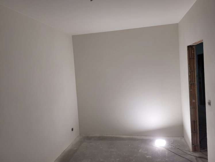 Wnętrze po gładziowaniu ścian i sufitu, widoczne ślady po szlifowaniu, surowa ościeżnica drzwiowa, lampa podłogowa oświetla pomieszczenie.