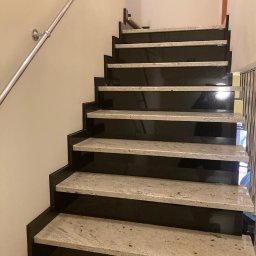 A&M System - Schody z czarnego granitu z jasnymi stopniami i metalową poręczą, widok z dołu, oświetlenie górne.