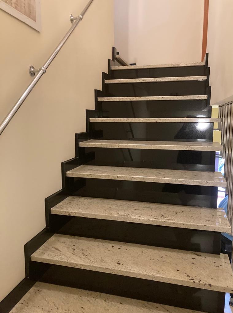 Schody z czarnego granitu z jasnymi stopniami i metalową poręczą, widok z dołu, oświetlenie górne.