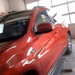 Dawid Salicki - Czerwony SUV na podnośniku w warsztacie. Widoczne odbicia światła na karoserii, podkreślające świeżość lakieru. Auto po blacharce/lakierowaniu, gotowe do odbioru.