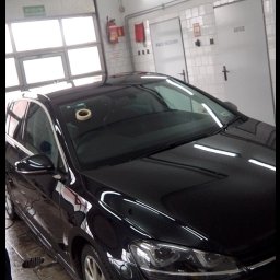 Dawid Salicki - Błyszczący, czarny samochód w warsztacie blacharsko-lakierniczym, z taśmą maskującą na dachu. Widoczne płytki na ścianach i podłodze, oświetlenie warsztatowe.