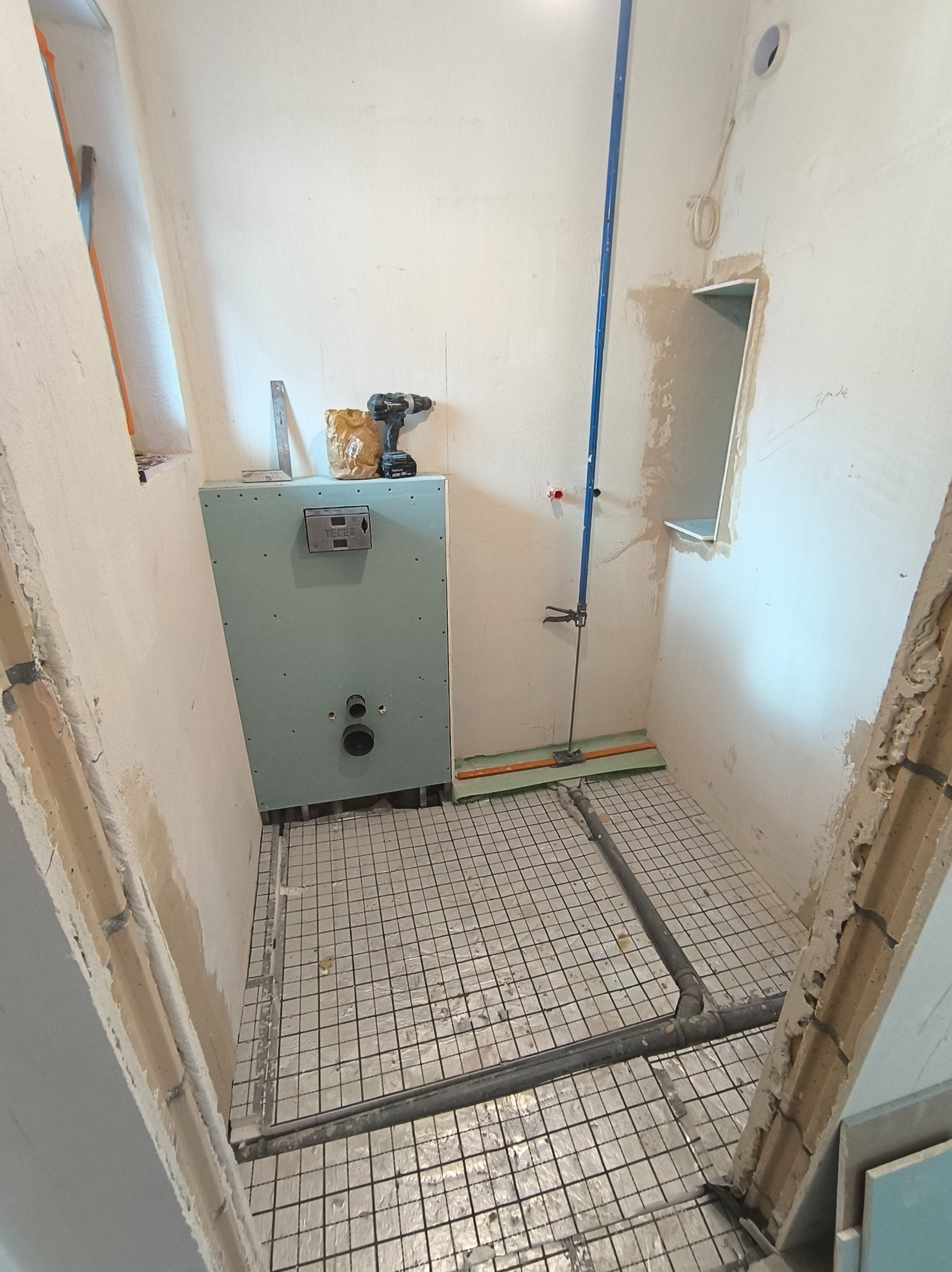 Instalacja ogrzewania podłogowego w łazience, widoczny stelaż podtynkowy WC, narzędzia i elementy instalacji. Etap prac wykończeniowych, surowe ściany.