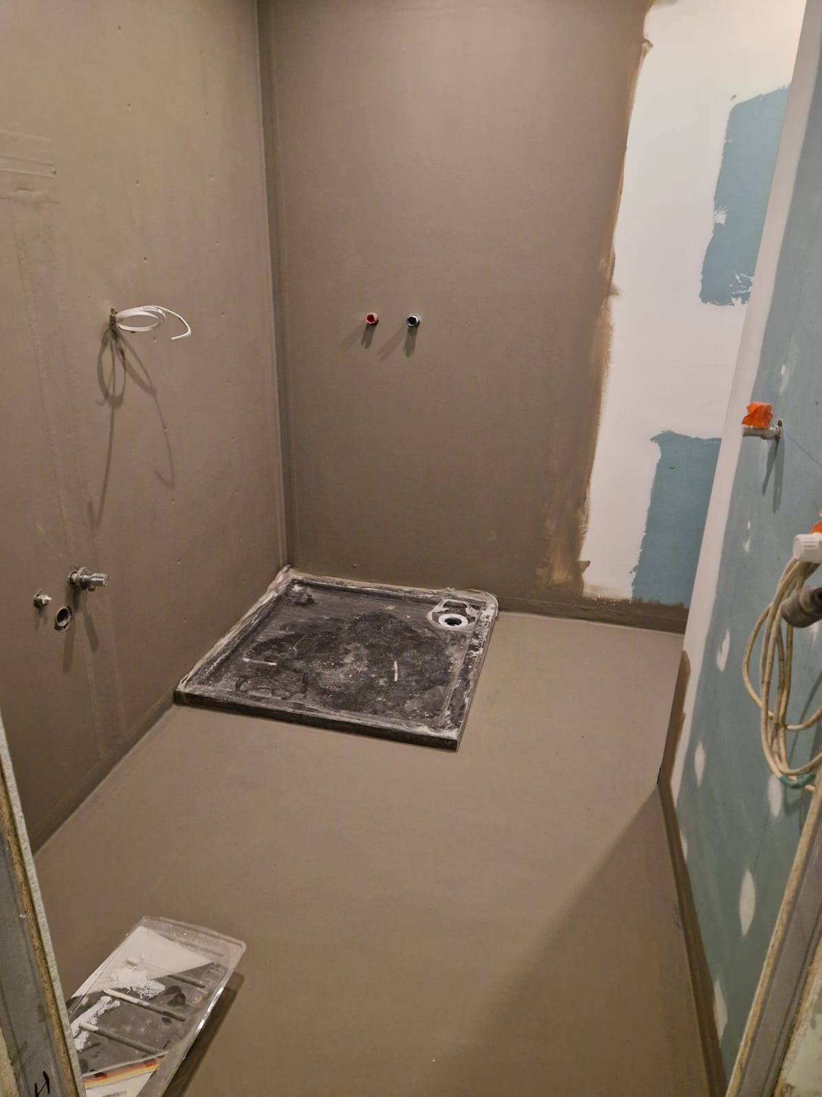 Przygotowana do wykończenia łazienka z brodzikiem, świeżo wylana wylewka, ściany przygotowane pod płytki, widoczne instalacje wodne i elektryczne.