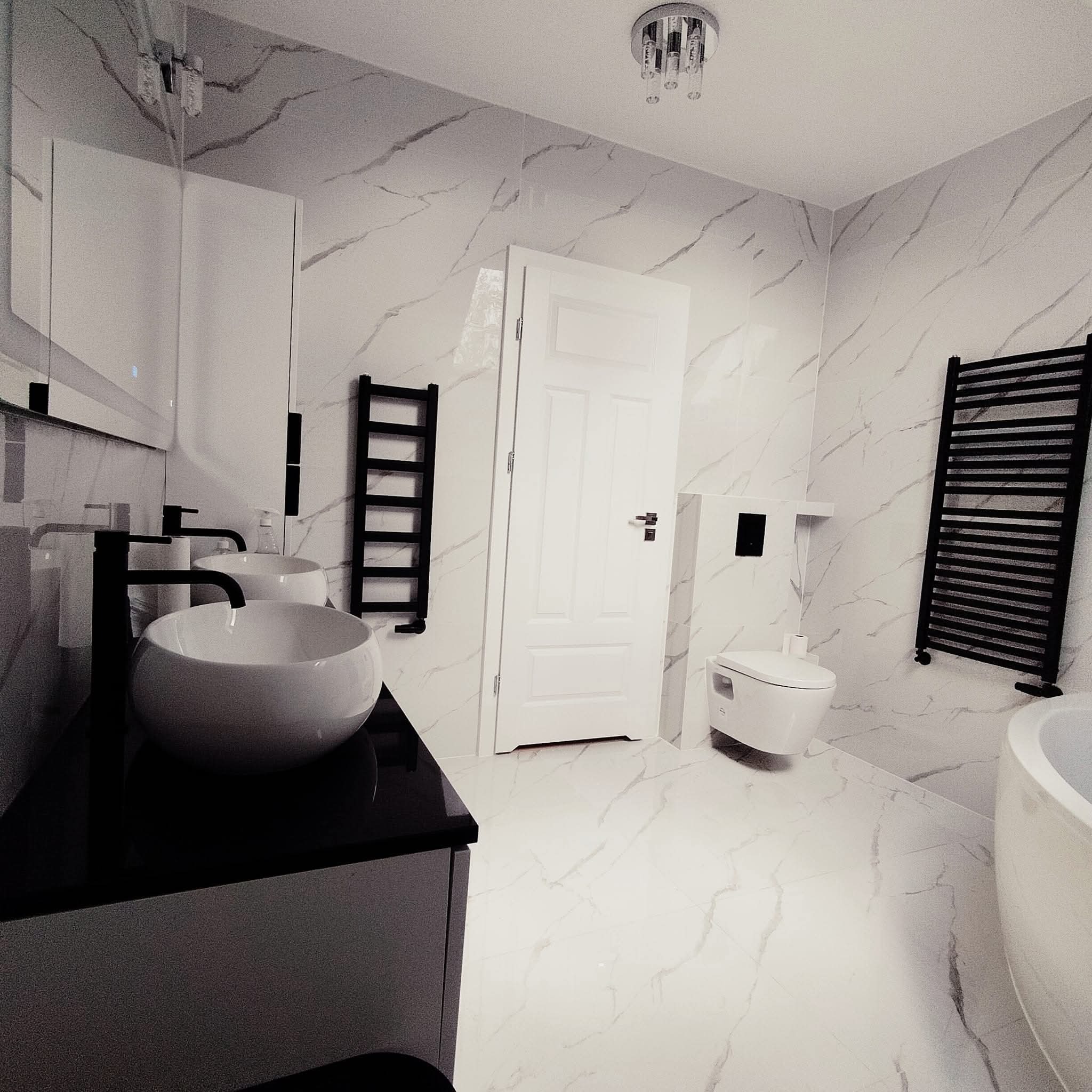 Elegancka łazienka z marmurowymi płytkami, umywalkami nablatowymi i czarnymi grzejnikami drabinkowymi. Nowoczesne oświetlenie sufitowe.