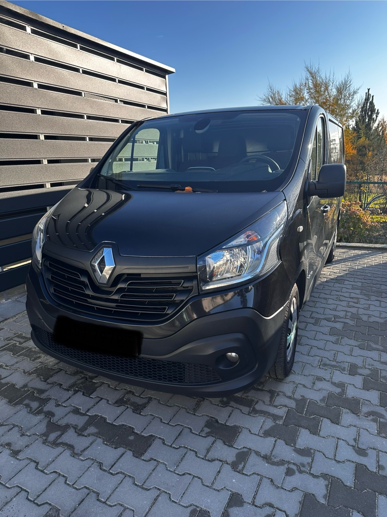 Czarny van Renault na kostce brukowej, zaparkowany przed nowoczesnym ogrodzeniem. Pojazd gotowy do transportu podczas opróżniania mieszkania.