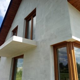 Docieplenia Elewacje Wojciech - Nowoczesny dom z jasną elewacją o fakturze baranka i drewnianymi oknami. Widok z dołu, podkreślający bryłę budynku i detale wykończenia.