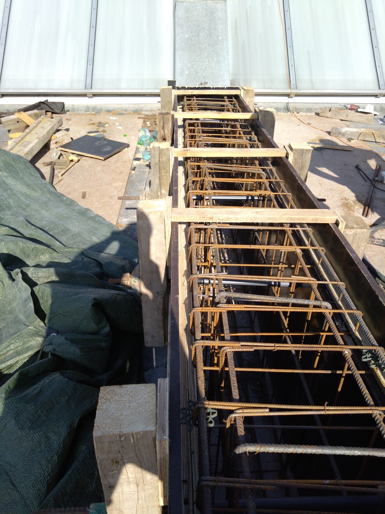 Zbrojenie w szalunku, widok z góry. Stalowe pręty tworzą siatkę wzmacniającą konstrukcję. Drewniane elementy podtrzymują formę. Etap budowy budynku żelbetowego.