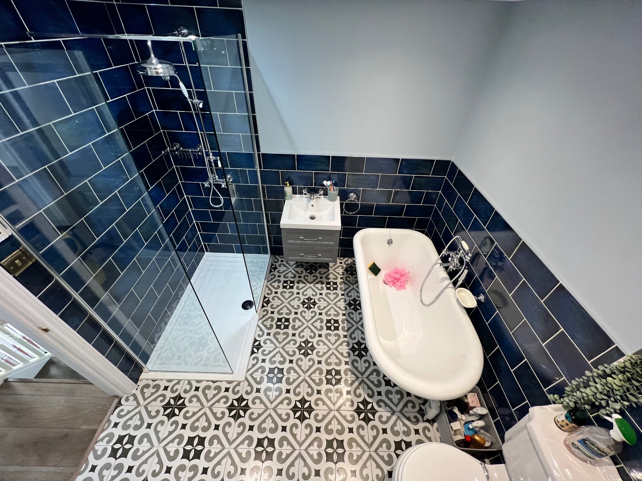 Wykończona łazienka we Włoszczowie z kabiną prysznicową, wanną na nóżkach i wzorzystą podłogą. Ciemne płytki na ścianach i jasne ściany tworzą kontrast.