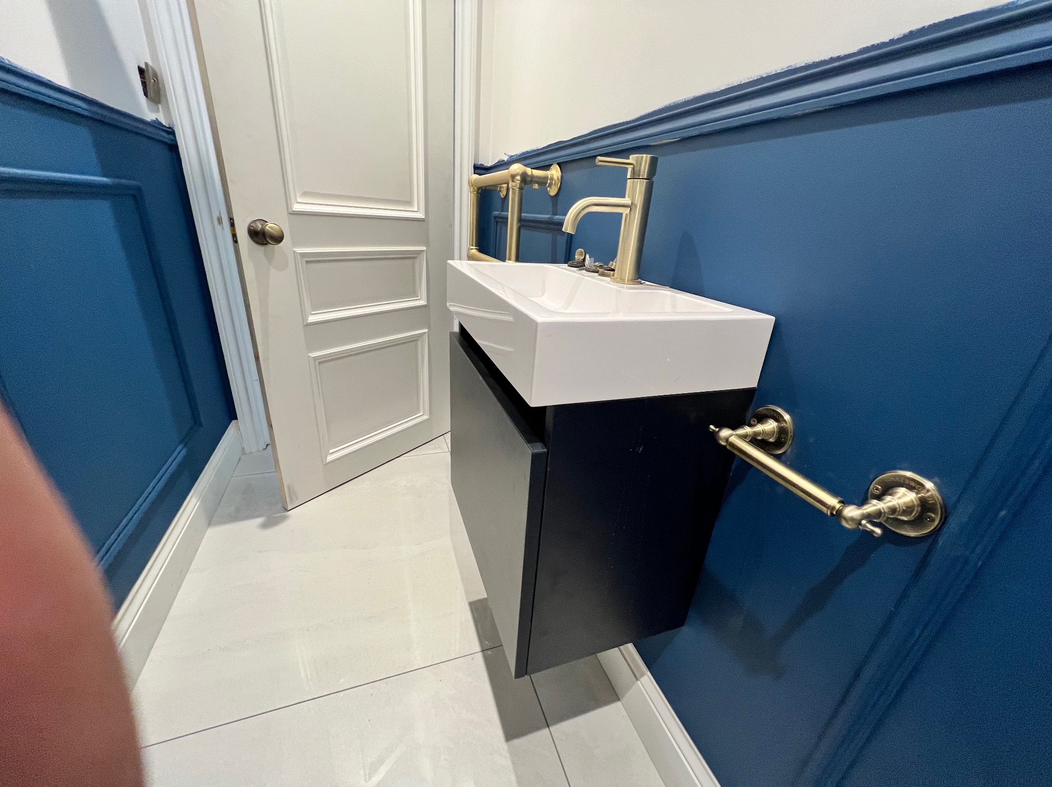 Nowoczesna łazienka: biała umywalka nablatowa z czarną szafką, złota armatura i akcesoria na tle granatowej ściany z dekoracyjnymi listwami.