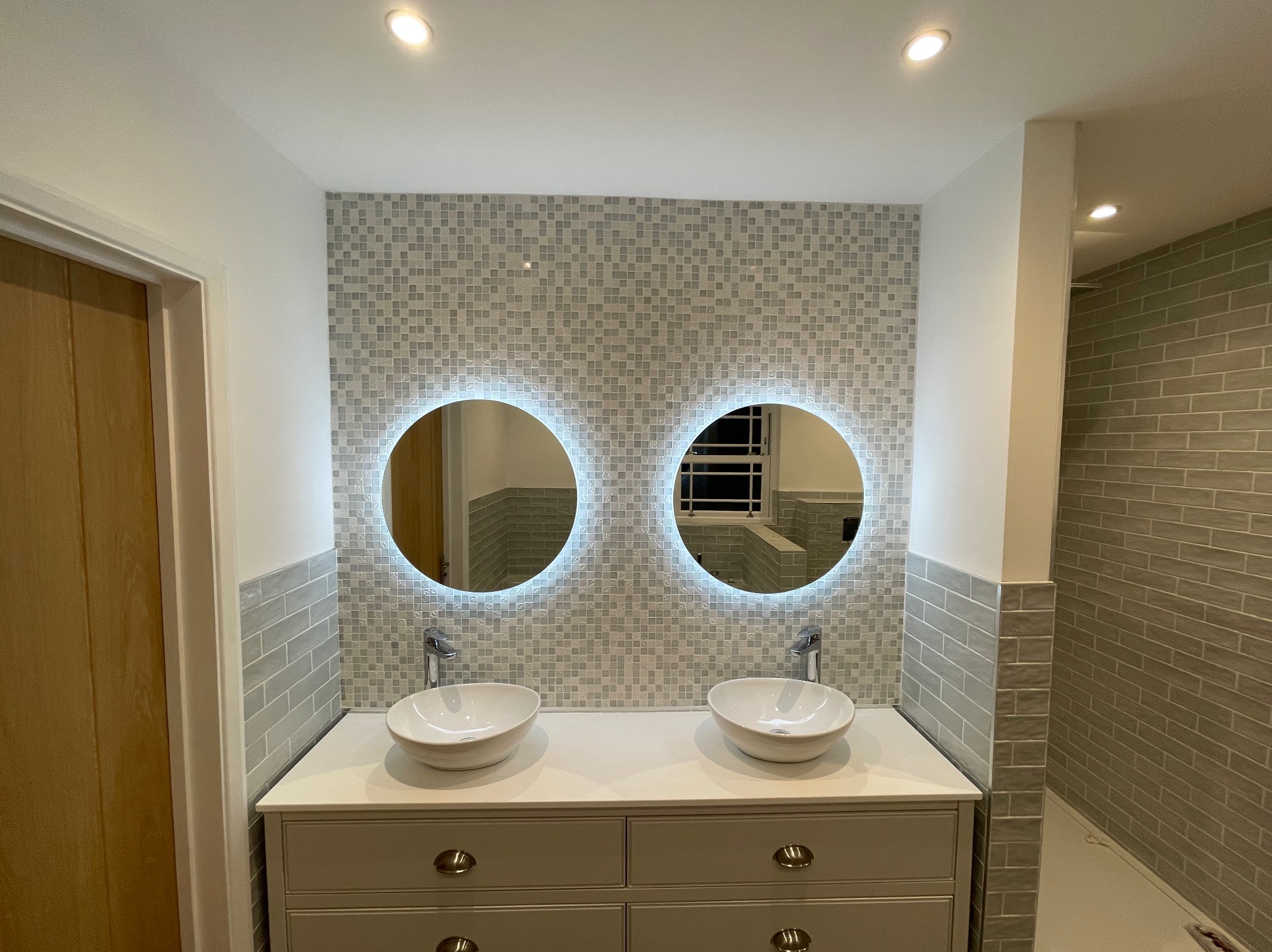 Wykończona łazienka w Oświęcimiu: dwie umywalki nablatowe, okrągłe lustra z podświetleniem LED i mozaika na ścianie. Nowoczesny design.