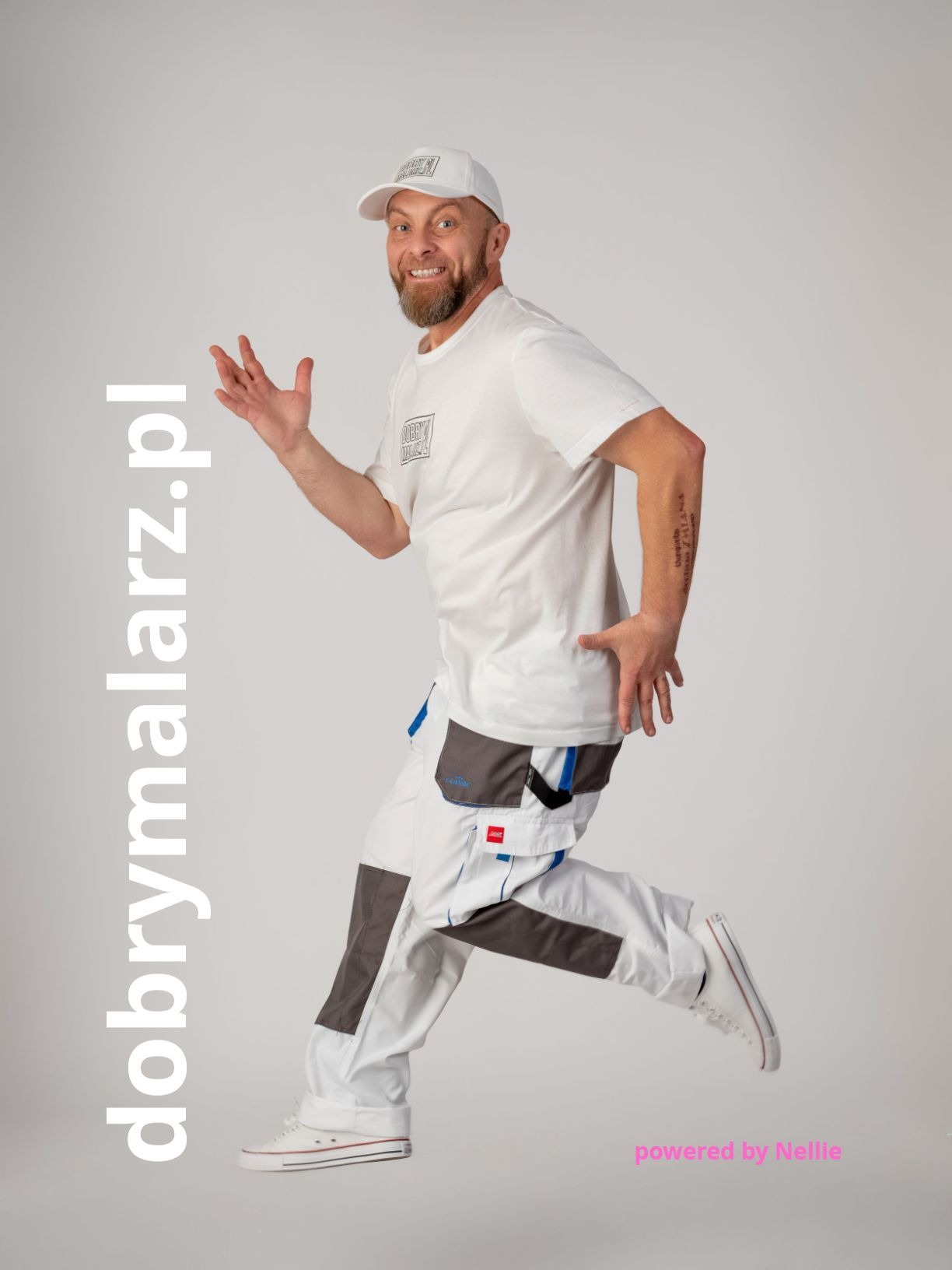 Uśmiechnięty malarz z Białegostoku w białym stroju roboczym w skoku, prezentujący firmę. Widoczne logo na koszulce i czapce, jasne tło.