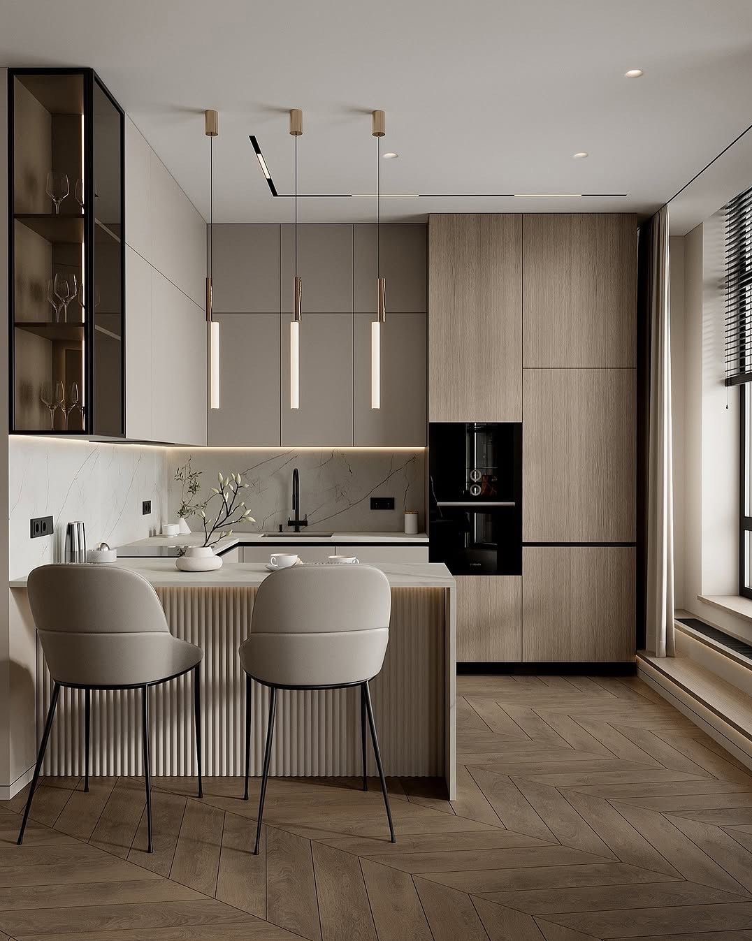 Nowoczesna kuchnia z drewnianą podłogą w jodełkę, beżowymi szafkami i marmurowym blatem. Dwa krzesła barowe stoją przy wyspie. Minimalistyczne lampy wiszą nad blatem.