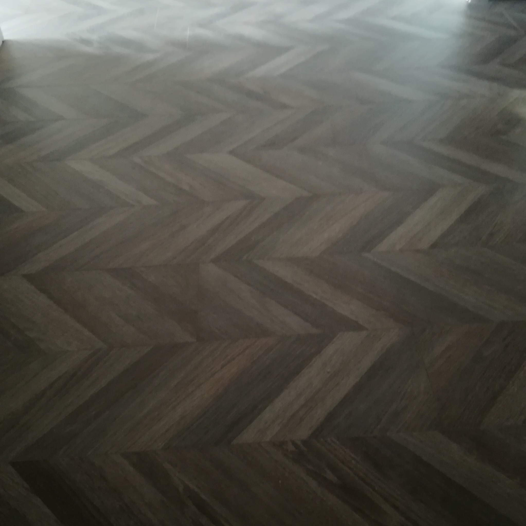 Ukończona podłoga z ciemnego drewna ułożona we wzór jodełki francuskiej, widok z góry, delikatne refleksy światła podkreślają strukturę drewna.