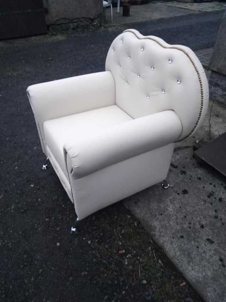 Biały fotel z oparciem w kształcie serca, zdobiony kryształkami i srebrną lamówką, stoi na zewnątrz. Nietypowy design i wykończenie.