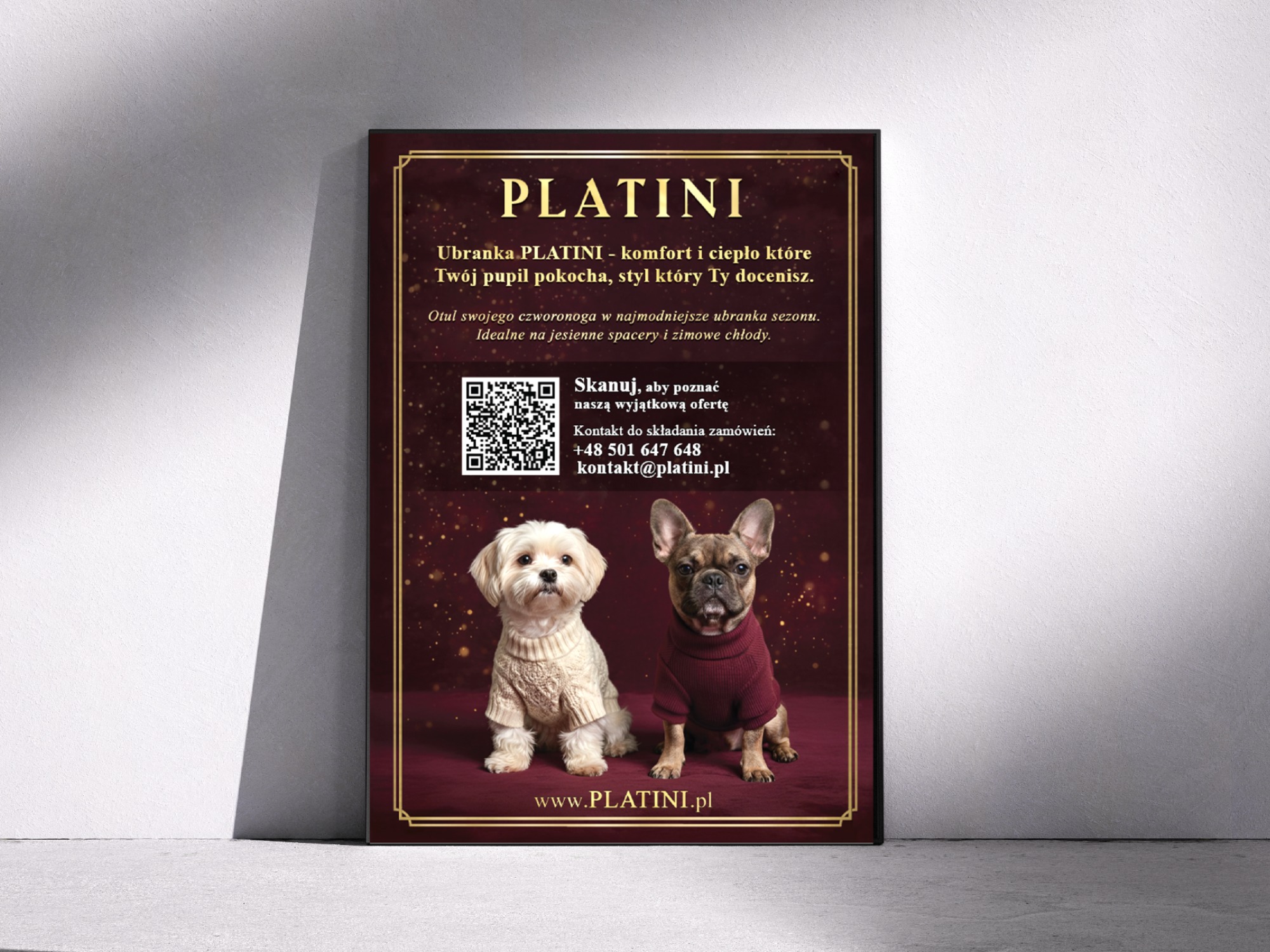 Plakat reklamowy z dwoma psami w ubraniach marki PLATINI na bordowym tle z złotymi akcentami, umieszczony na białej ścianie. Widoczny kod QR i adres strony internetowej.