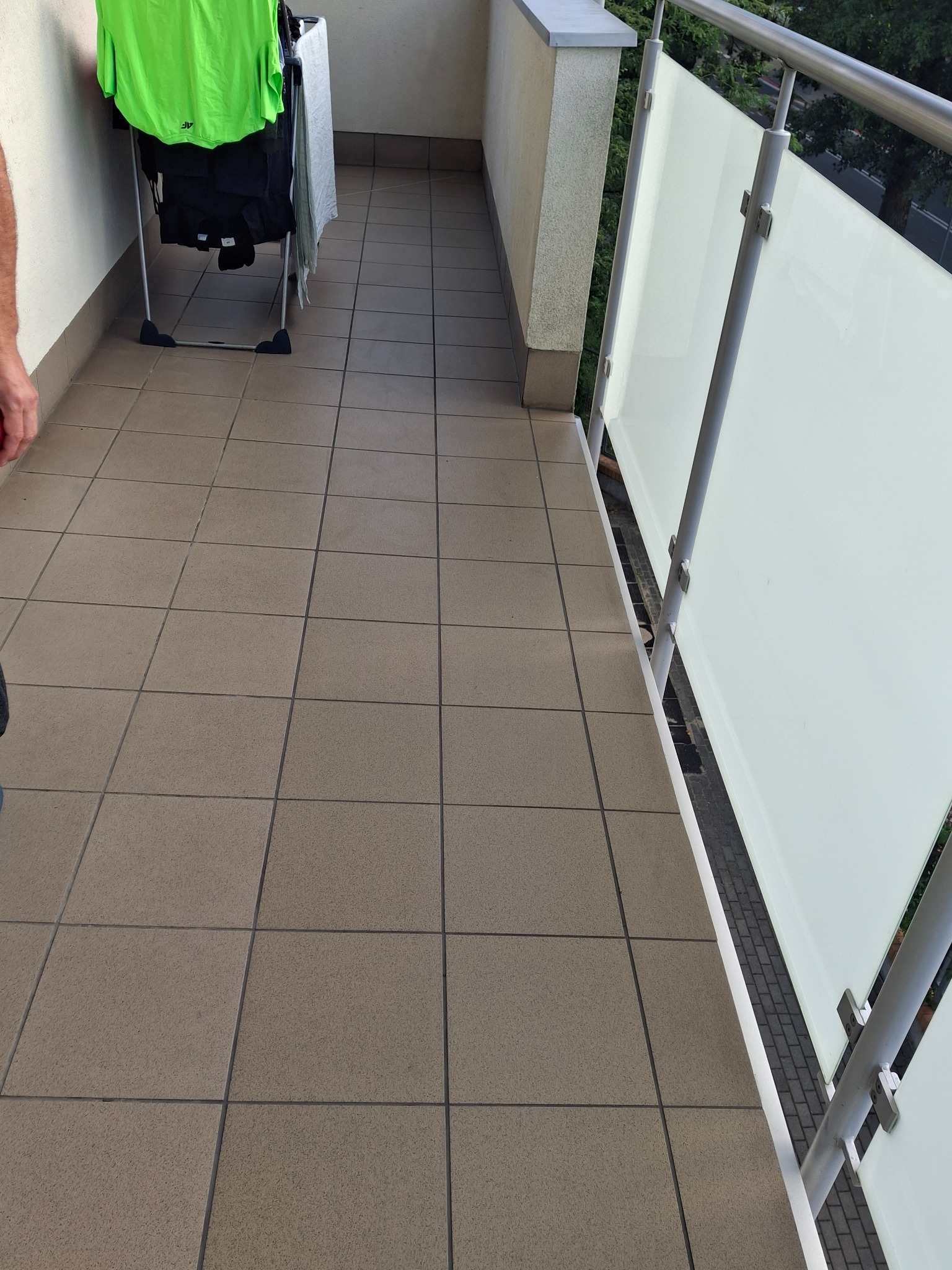 Wyłożony brązowymi płytkami balkon z białą balustradą i suszarką na ubrania. Widok z góry, ukazujący regularny wzór płytek i minimalistyczny design balustrady.