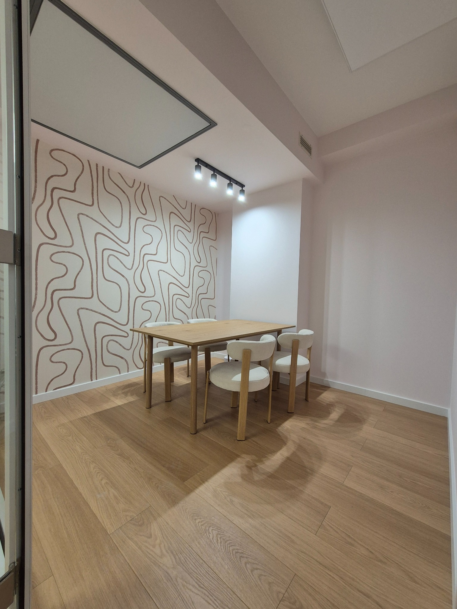 Jasne panele podłogowe, stół z krzesłami i dekoracyjna ściana w minimalistycznym biurze. Nowoczesne oświetlenie sufitowe.