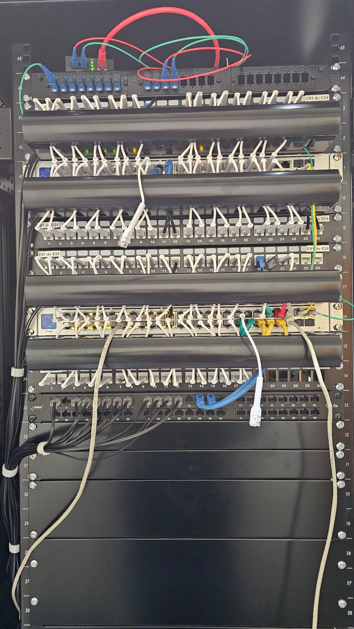 Panel krosowniczy z kablami sieciowymi w szafie rack, uporządkowane okablowanie w Będzinie. Widoczne porty i oznaczenia kabli.