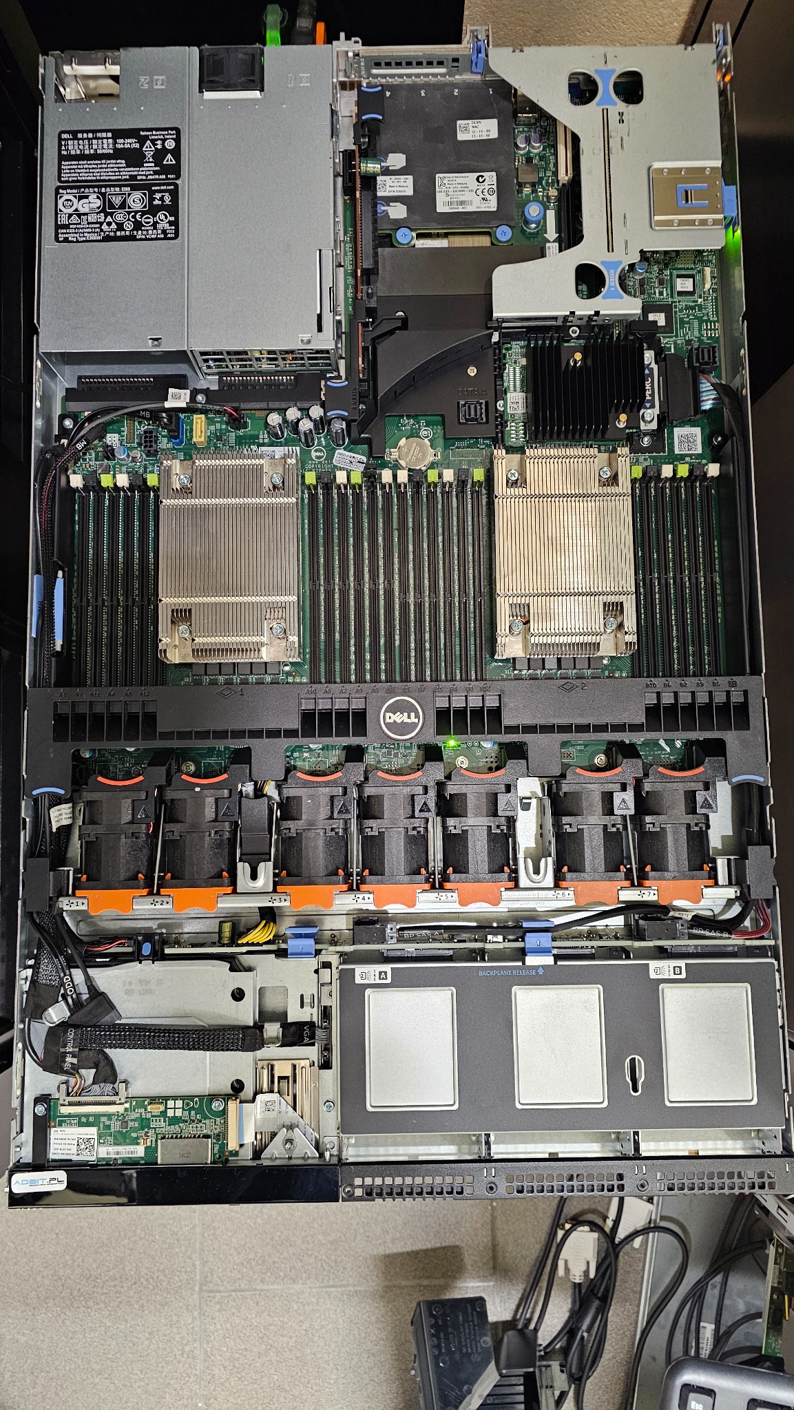 Wnętrze serwera Dell z widocznymi procesorami, pamięcią RAM, wentylatorami i zasilaczem. Widok z góry na otwartą obudowę. Elementy elektroniczne i kable wewnątrz.