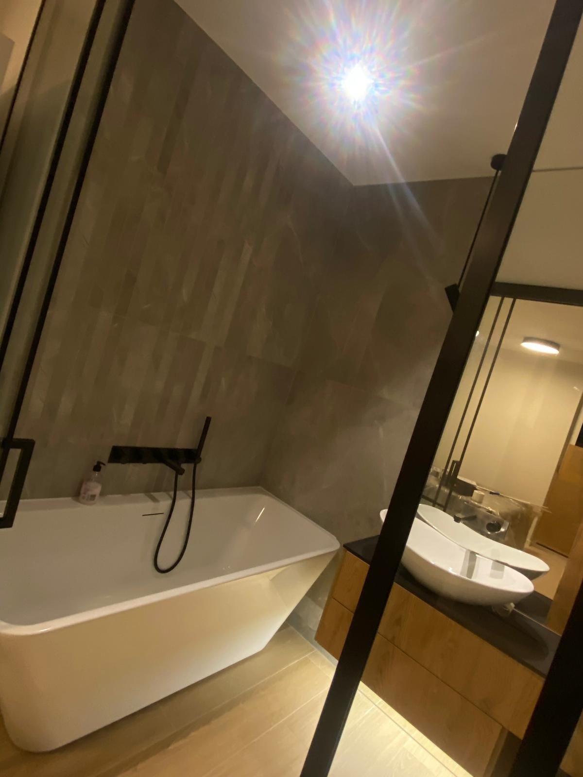 Nowoczesna łazienka z wolnostojącą wanną, umywalką nablatową i szarą, marmurkową okładziną ścienną. Widoczne czarne baterie i elementy wykończenia.