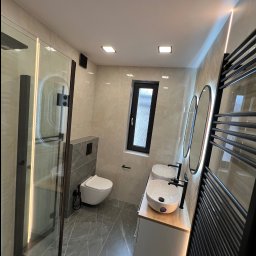 Ra2ns Building - Nowoczesna łazienka z kabiną prysznicową typu walk-in, podwójną umywalką nablatową i grzejnikiem drabinkowym w czarnym kolorze. Uwagę zwraca wąskie okno i oświetlenie LED.