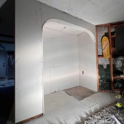 Szymon Różański SELF-MADE - Wnętrze w trakcie prac: ściany obłożone płytami karton-gips z łukowatym przejściem. Widoczne narzędzia i fragmenty instalacji. Surowy stan wykończenia.