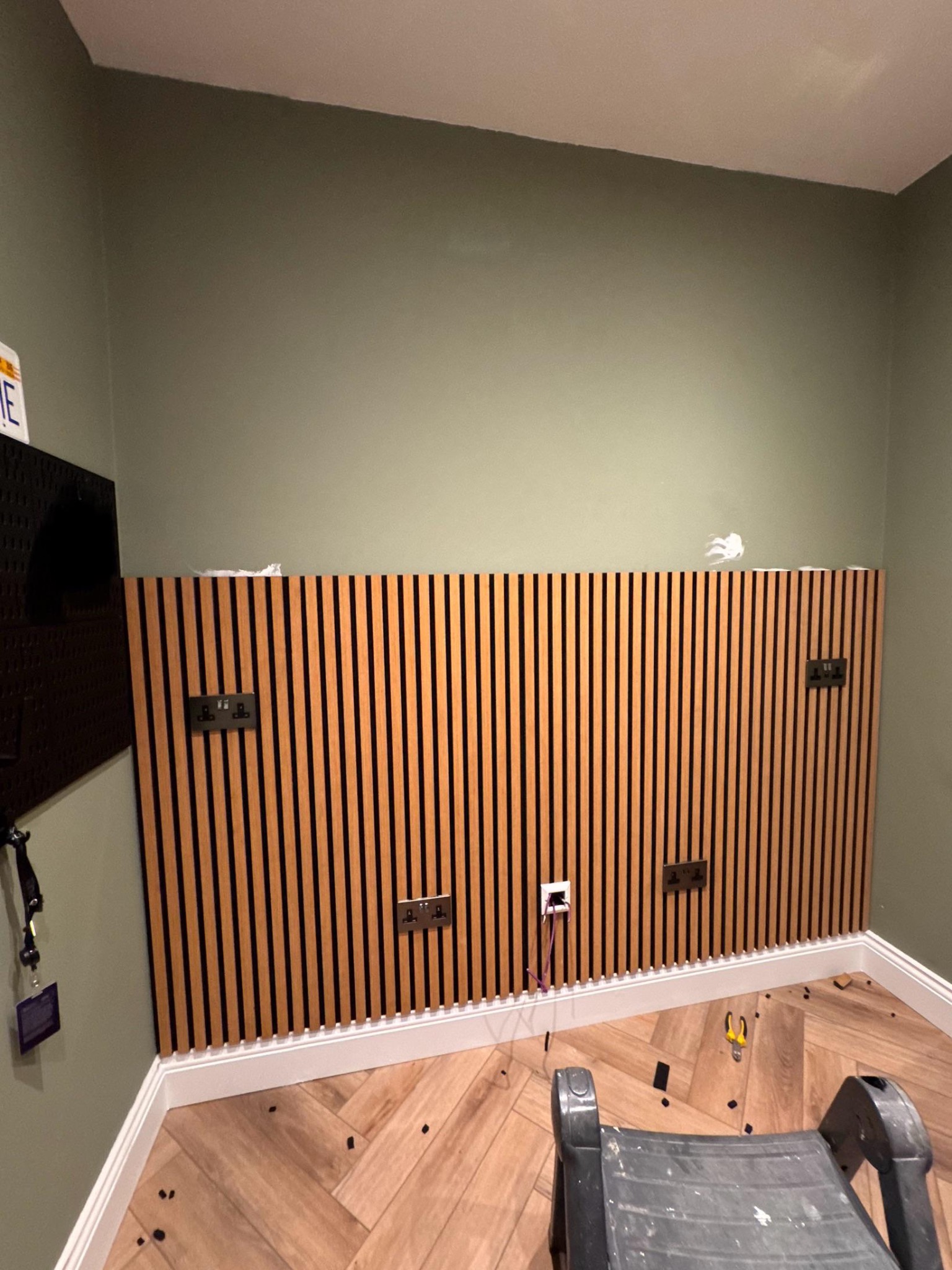 Drewniana lamelowa ściana z gniazdkami elektrycznymi w Prudniku. Widoczna podłoga w jodełkę i drabina malarska. Nowoczesny design wnętrza z akcentem na naturalne materiały.