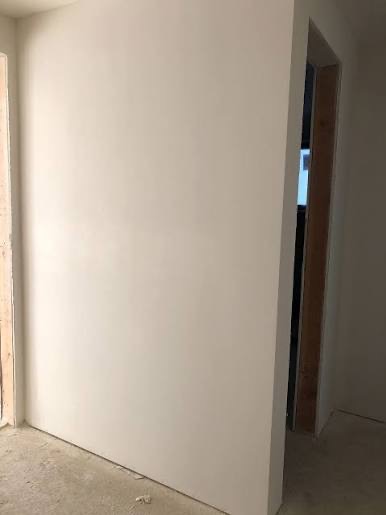 Gładka, świeżo wyszpachlowana ściana w jasnym odcieniu, widoczna w kadrze z fragmentem ościeżnicy drzwiowej. Minimalistyczne ujęcie, skupiające się na fakturze powierzchni.