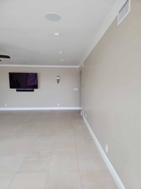 Jasne wnętrze po remoncie: beżowe ściany z listwami, płytki podłogowe, telewizor na ścianie, oświetlenie sufitowe. Minimalistyczny design, świeżo po wykończeniu.